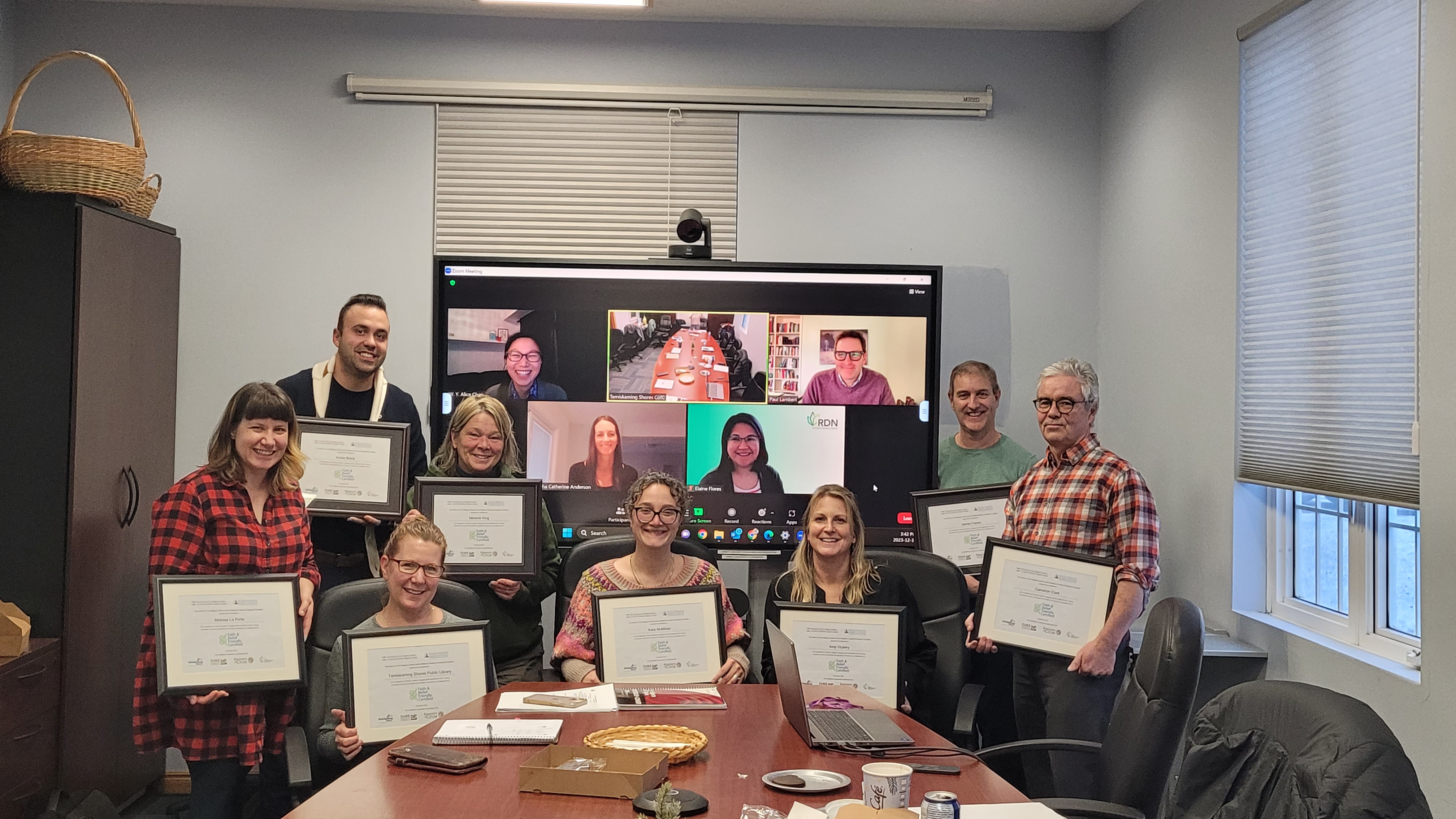 Une photo de huit personnes tenant leur certificat dans une salle de réunion, debout devant un écran qui montre six personnes souriantes.